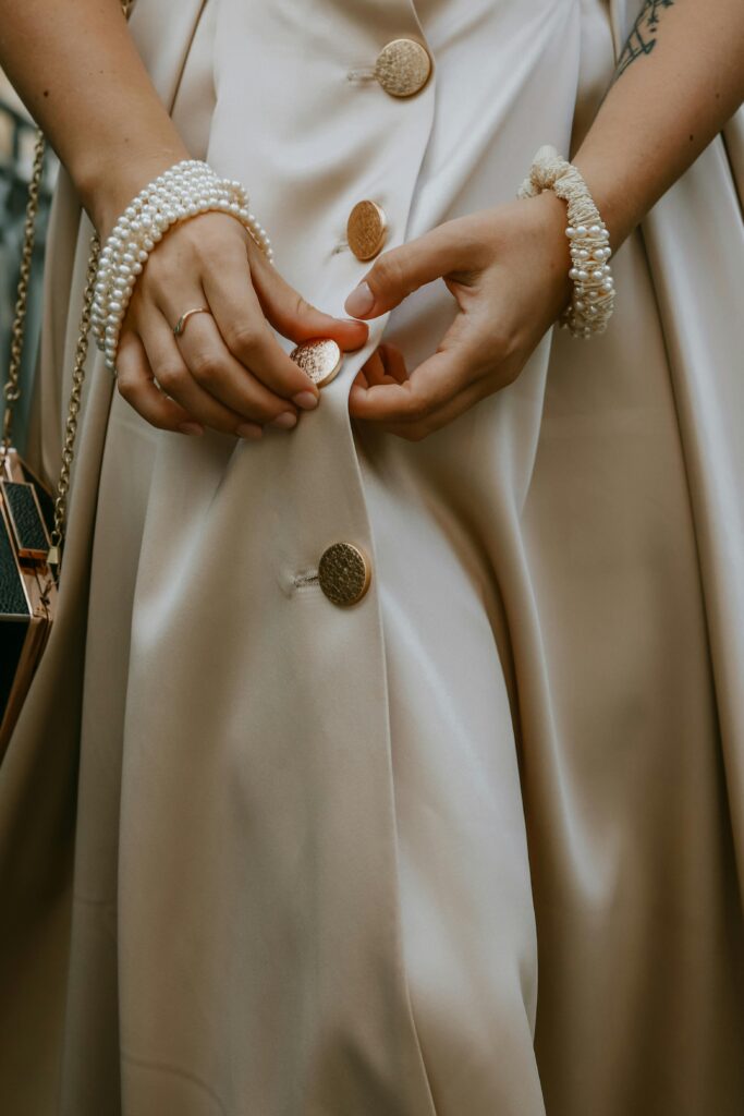 Close-up of a woman's hands adjusting buttons on a pearl-embellished dress, showcasing elegance and luxury.